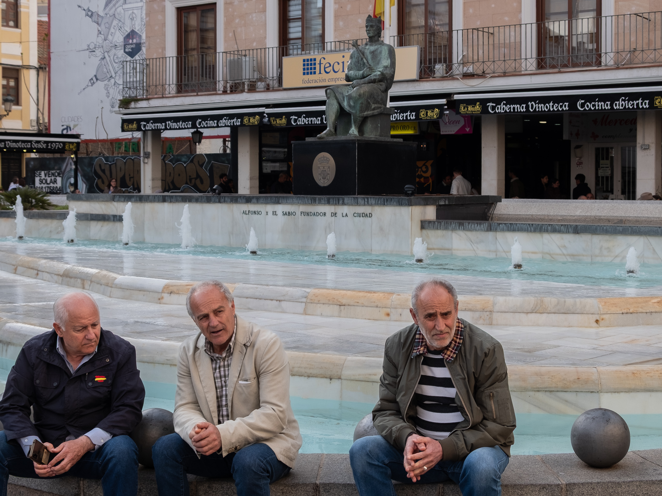 Drei Männer am Brunnen – Alfonso X el Sabio im Hintergrund